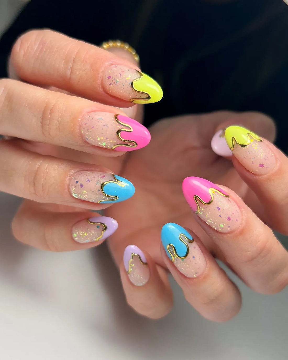 Handmade press-on nails with pastel neon drip design, gold accents, glitter flakes, almond shape