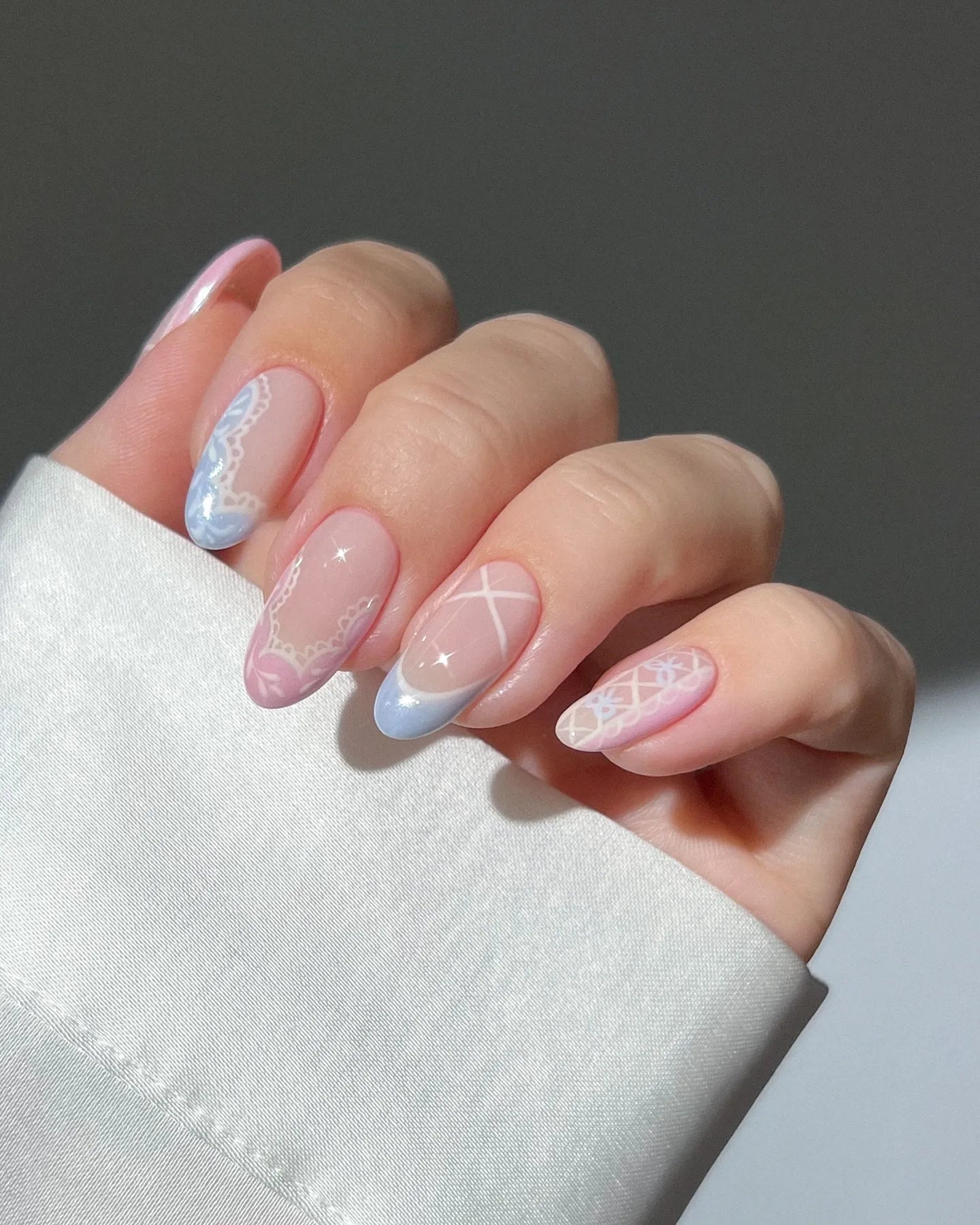Hand with pastel pink and blue lace heart press-on nails featuring elegant cottagecore designs.