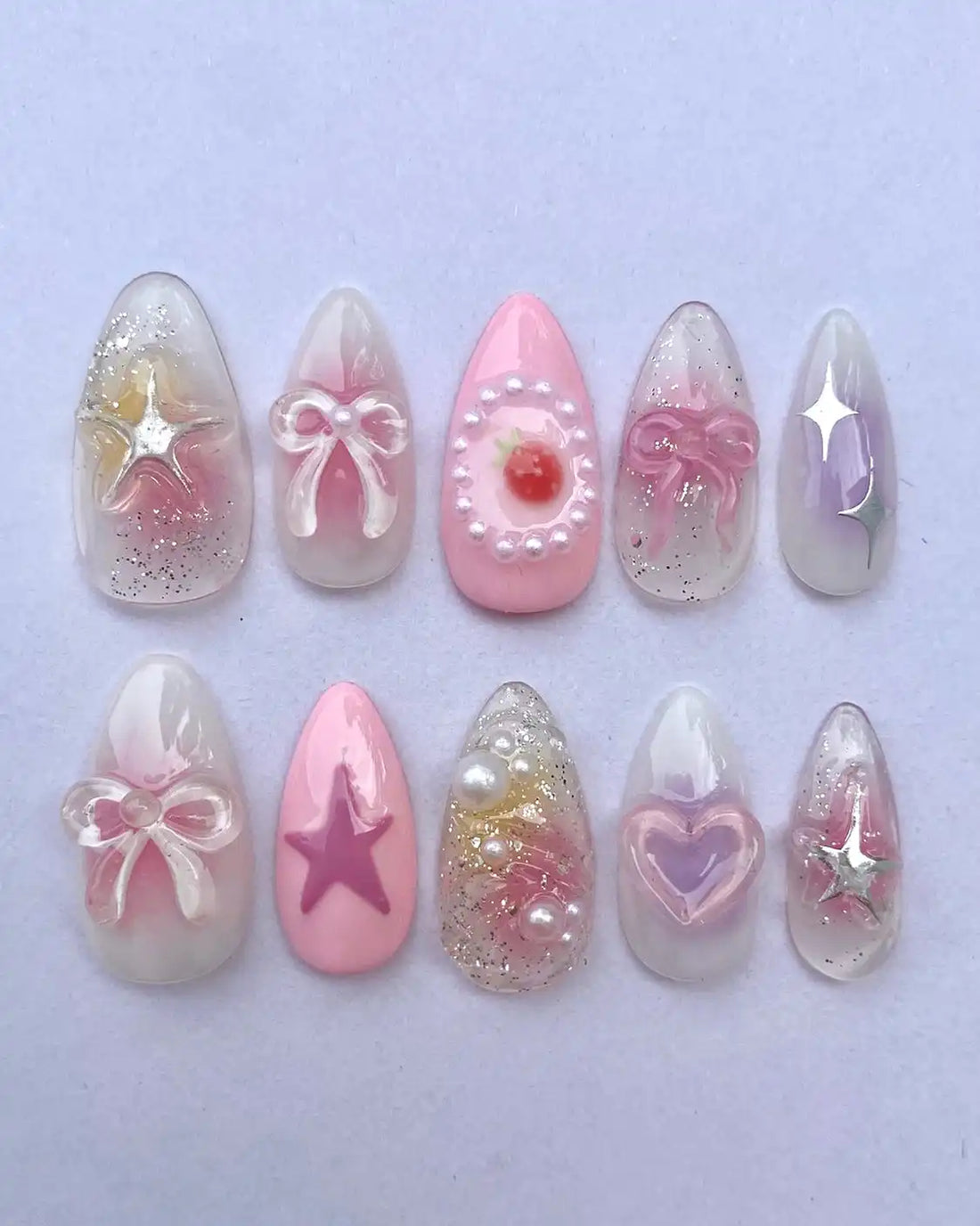 Handmade pastel pink press-on nails with stars, bows, hearts, pearls, and glitter accents.