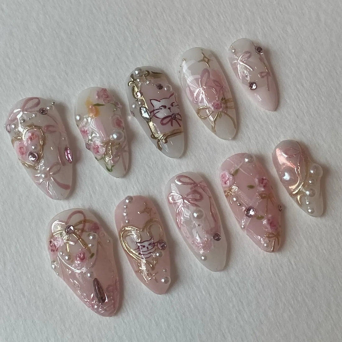 Handmade press-on nails with pink bows, cat design, roses, rose gold accents, and pearls.