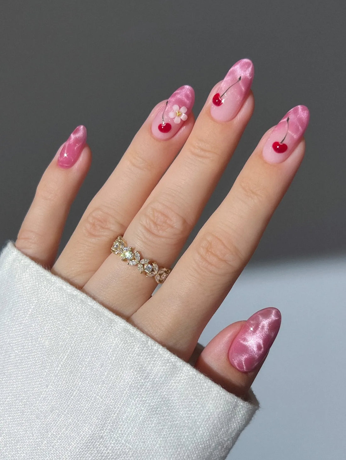 Hand with pink cat eye chrome press-on nails featuring cherry and flower kawaii designs