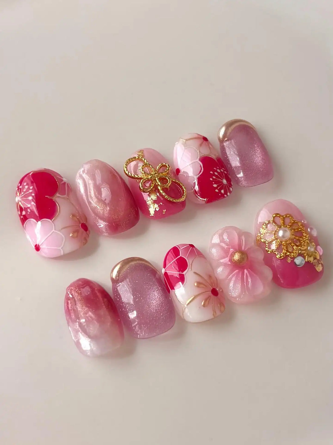 Handmade pink press-on nails with cherry blossom designs, gold charms, and shimmer accents.