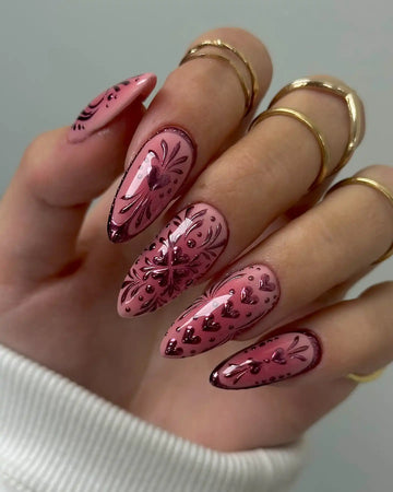 Hand showing long pink press-on nails with chrome heart and floral designs.