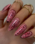 Hand with long pink chrome press-on nails featuring floral and heart designs, perfect for Valentine’s Day.