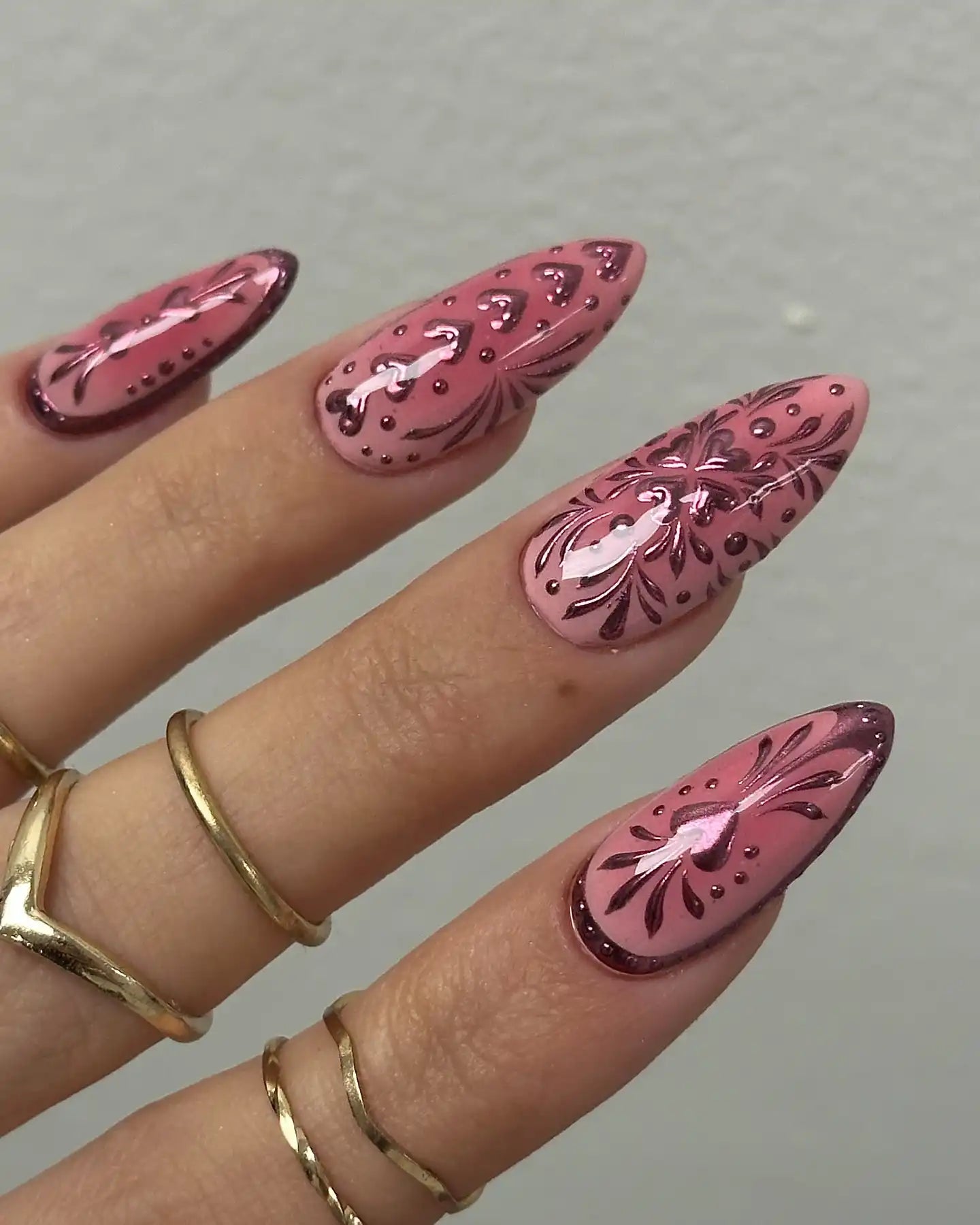 Hand with handmade pink chrome floral and heart press-on nails, almond shape, gold rings
