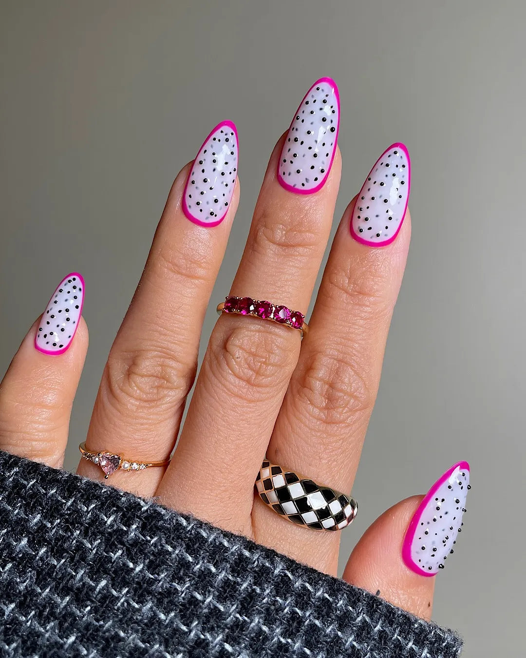 Hand with almond-shaped press-on nails featuring white base, black polka dots, and pink tips