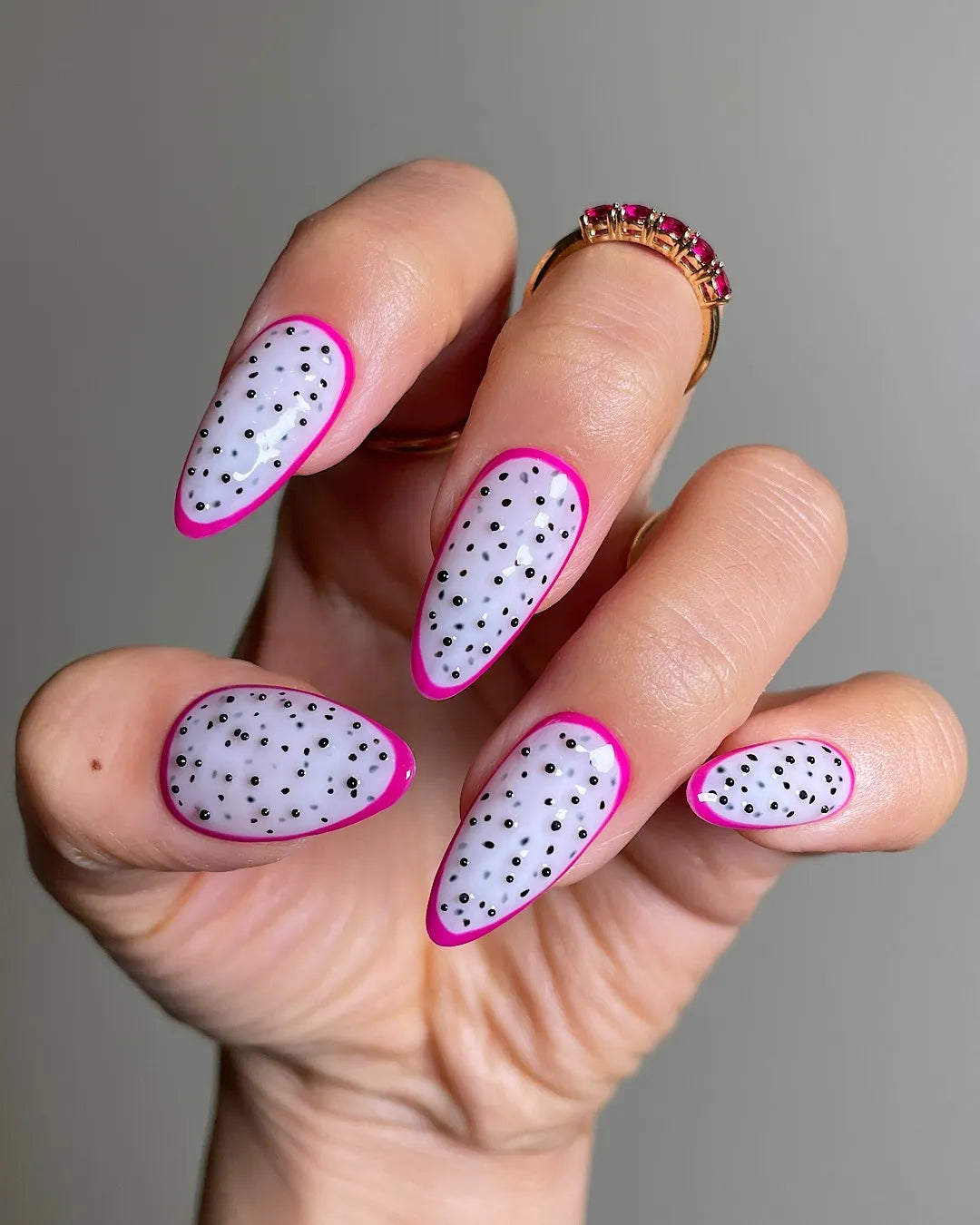 Hand with almond-shaped press-on nails featuring white base, black polka dots, and pink tips