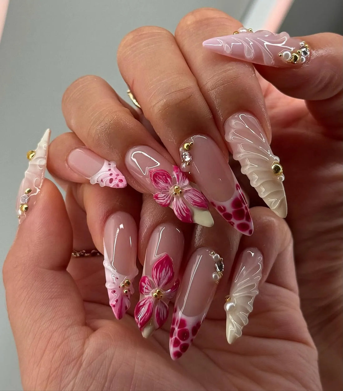 Hand with pink floral French swirl press-on nails, pearls, rhinestones, and elegant 3D accents.