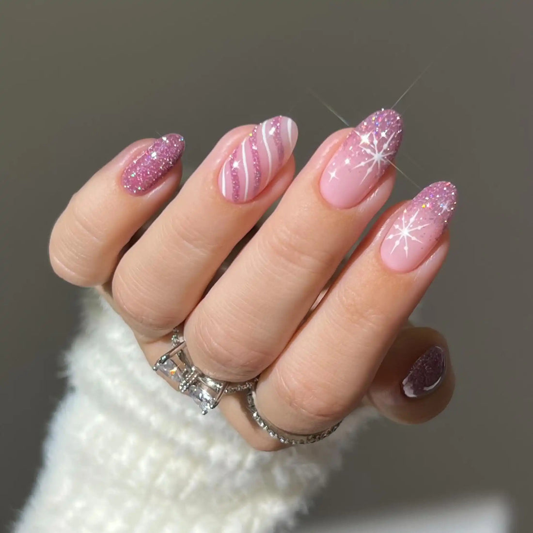 Hand wearing pink glitter ombre press-on nails with snowflake and stripe winter designs