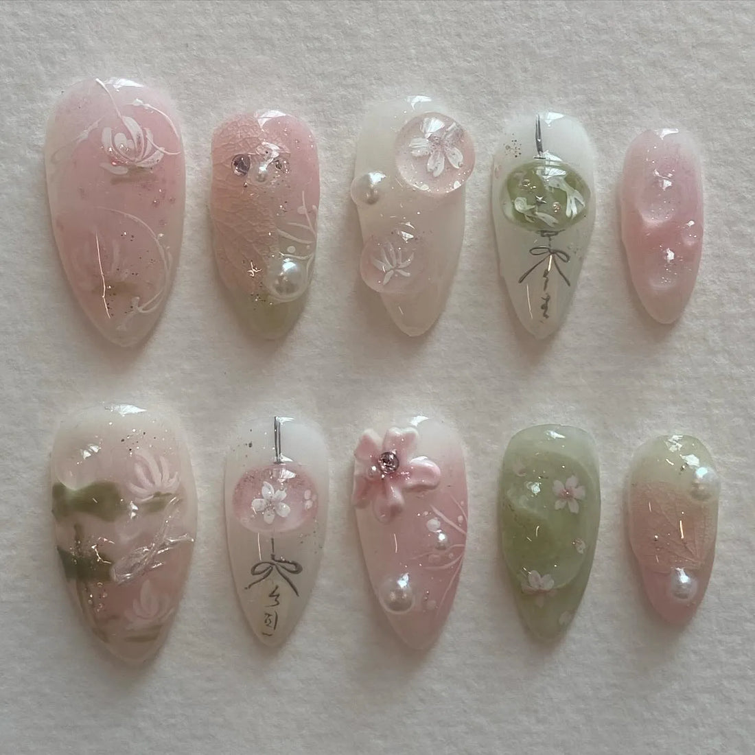 Handmade pink and green press-on nails with cherry blossom and pearl designs on a white background.