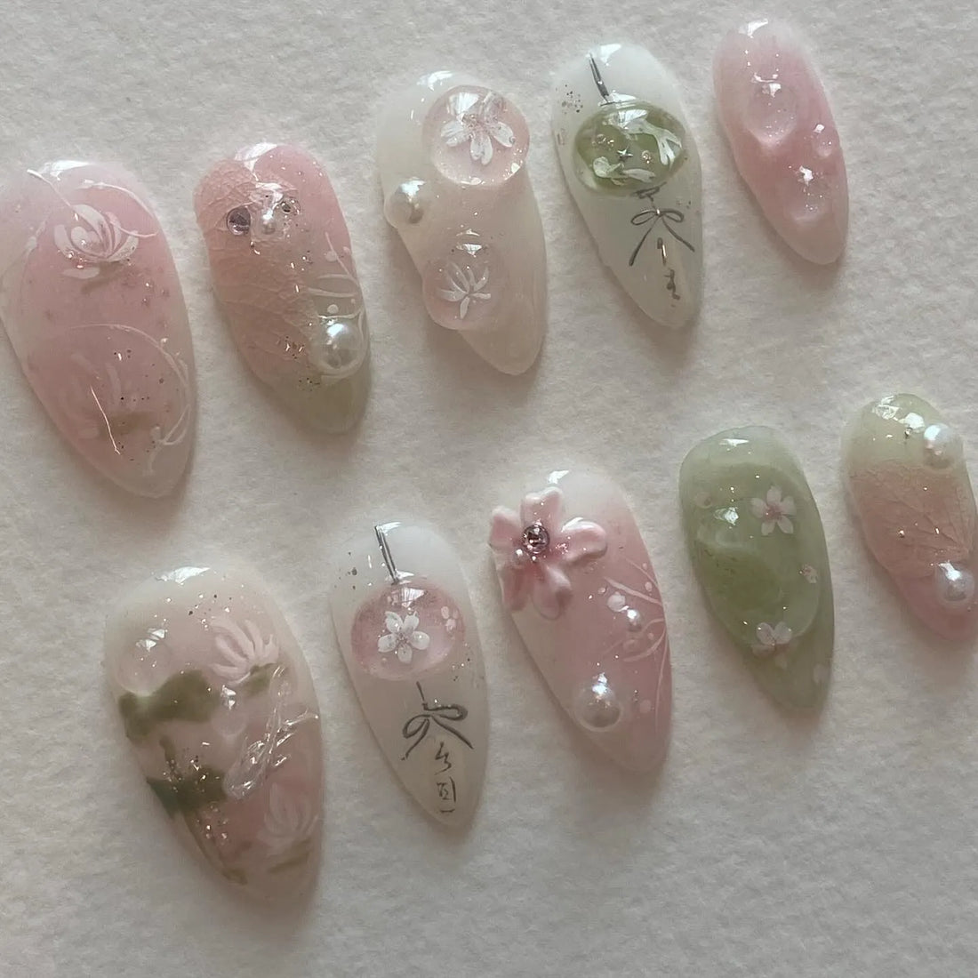 Handmade pink and green press-on nails with cherry blossom and pearl designs on a white background.