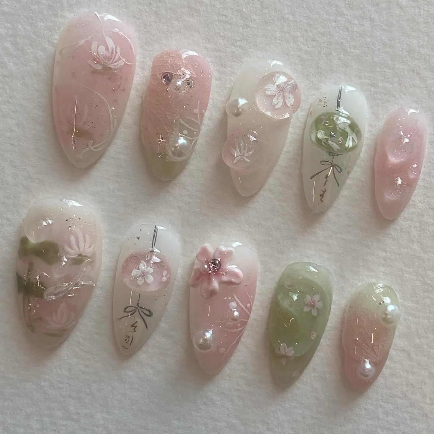 Handmade press-on nails with pink and green cherry blossom designs, pearls, and lantern art.
