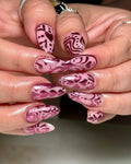 Handmade pink chrome press-on nails with metallic heart and folk art designs.