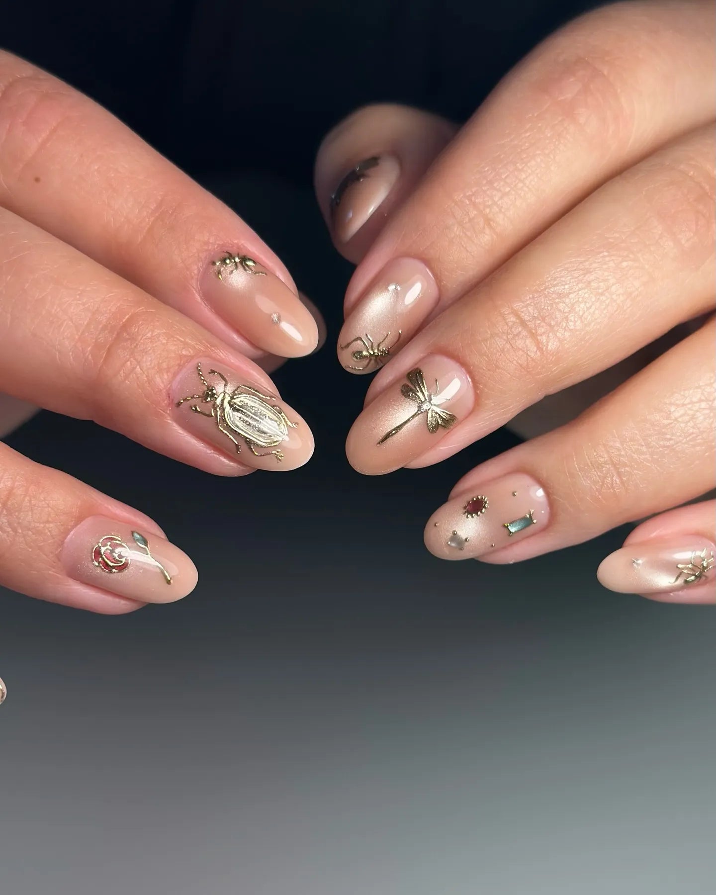 Handmade nude press-on nails with gold insect designs and gemstone accents.