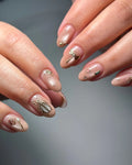 Handmade nude press-on nails with gold insect, flower, and gemstone designs