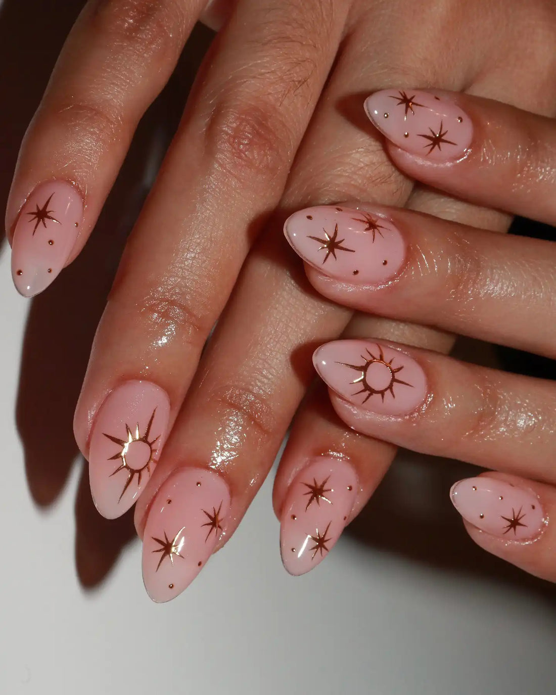 Hand with almond-shaped pink press-on nails featuring gold starburst and constellation designs.