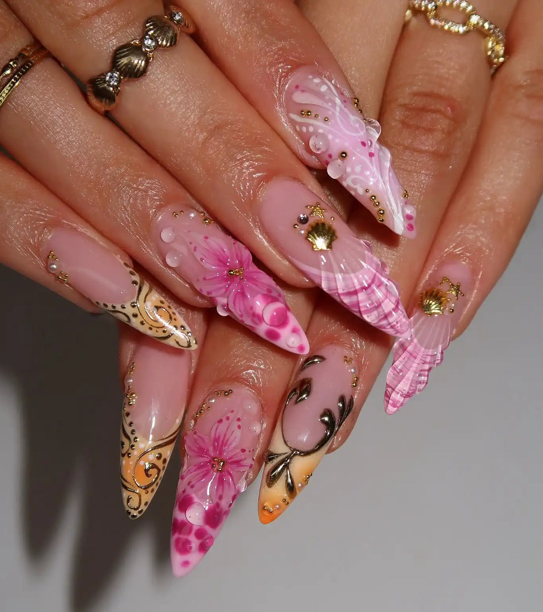 Handmade pink ombre press-on nails with gold seashell, floral, and water drop designs.