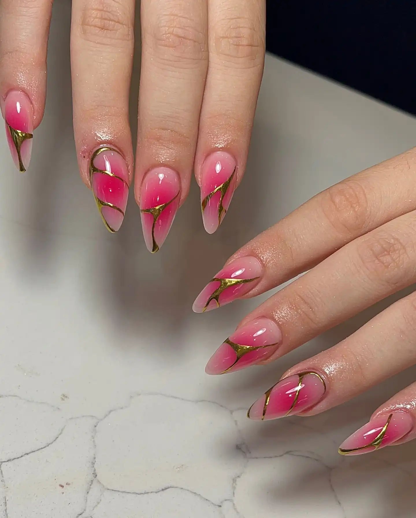 Hand with almond-shaped pink ombre press-on nails, gold lined edges, glossy finish