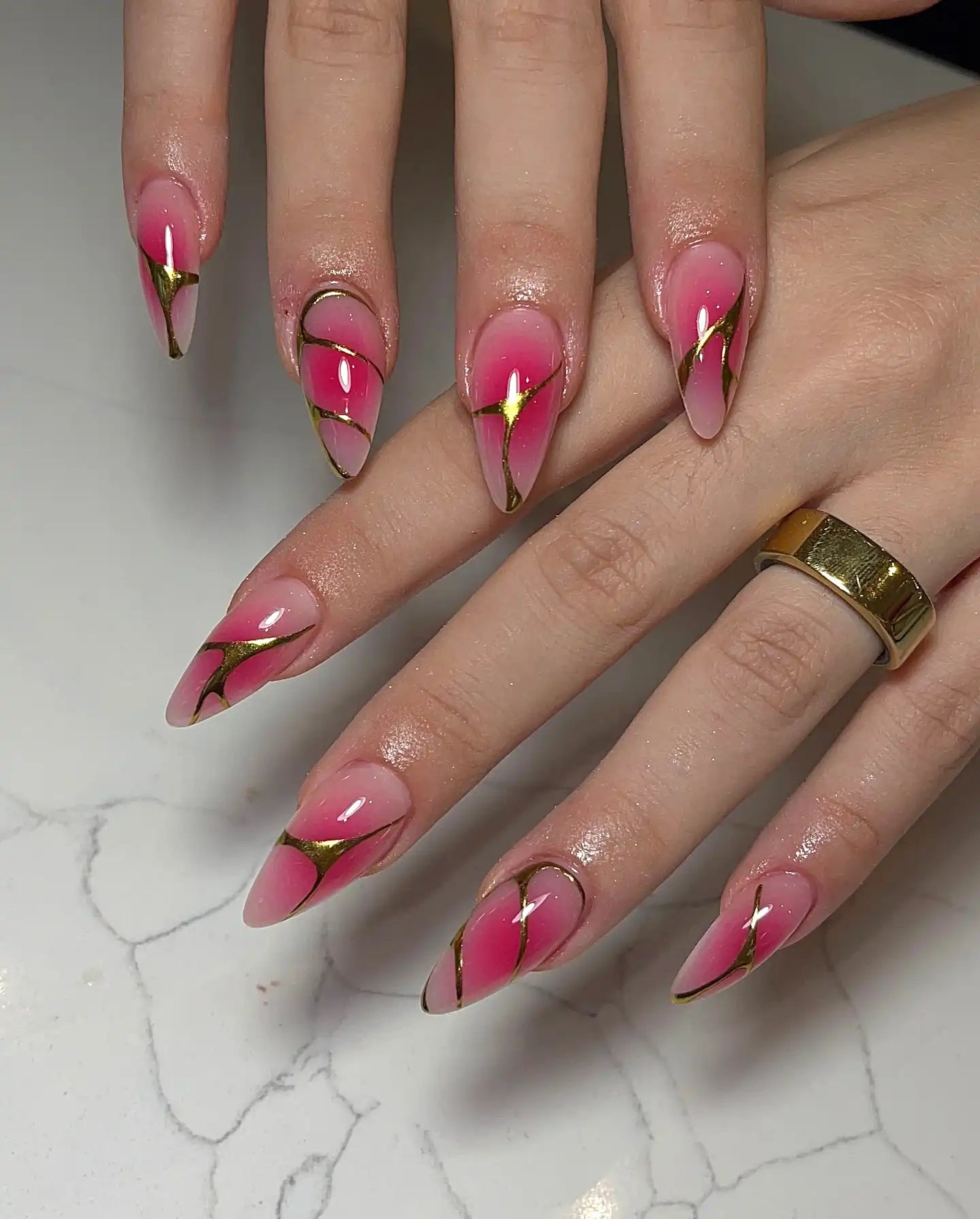 Hand with glossy pink ombre press-on nails featuring gold-lined edgy designs