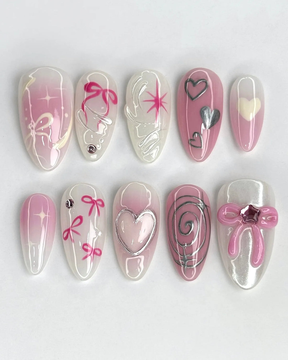 Handmade pink ombre press-on nails with silver metallic hearts, bows, and sparkly accents