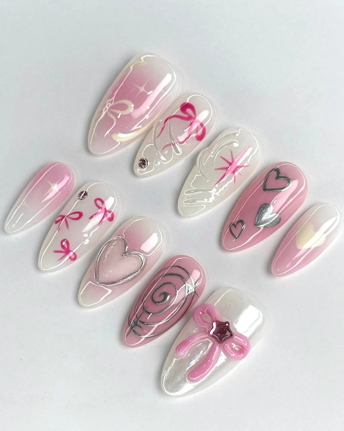 Handmade pink ombre press-on nails with silver metallic hearts, bows, and sparkly accents