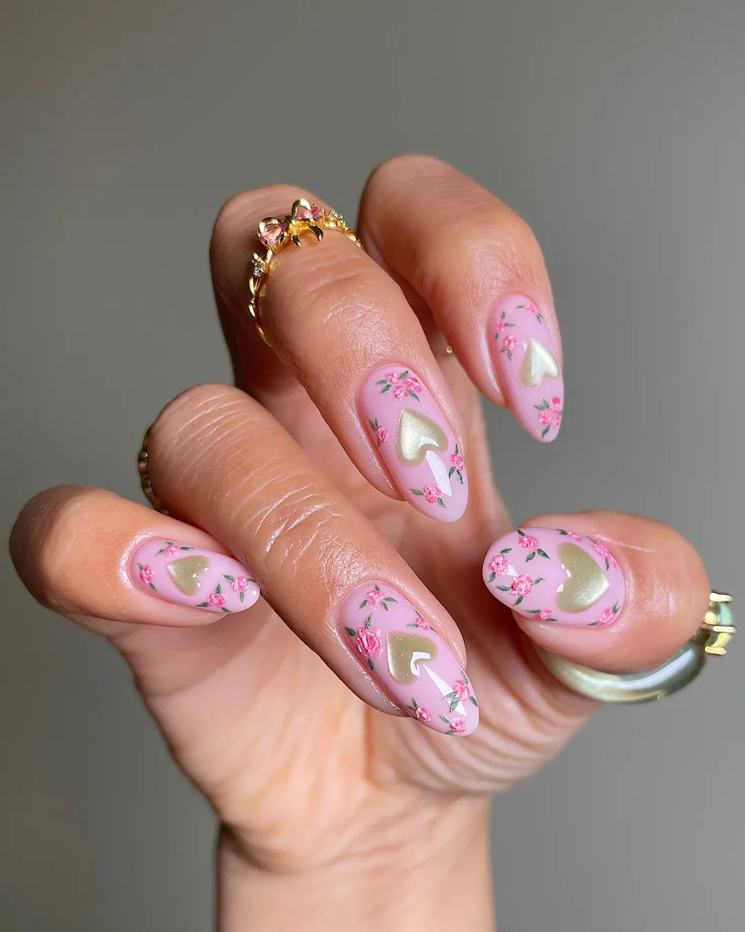 Hand with pink pastel press-on nails featuring gold hearts and floral designs