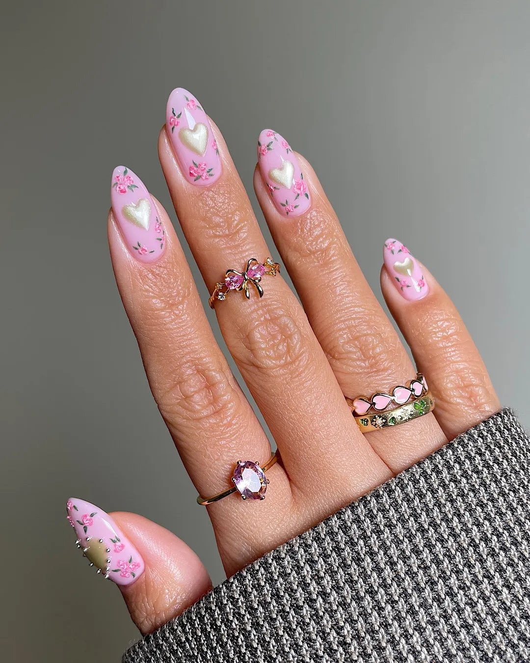Hand with pink pastel press-on nails featuring gold hearts and floral designs