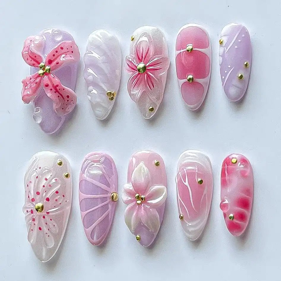 Handmade pink and purple press-on nails with 3D flower designs and gold accents on white background.