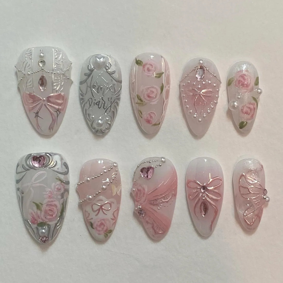 Handmade press-on nails with pink rose designs, silver baroque details, bows, and pearl chains