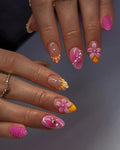Hand with pink shell press-on nails, 3D flower accents, pearls, and summer beach nail art design.