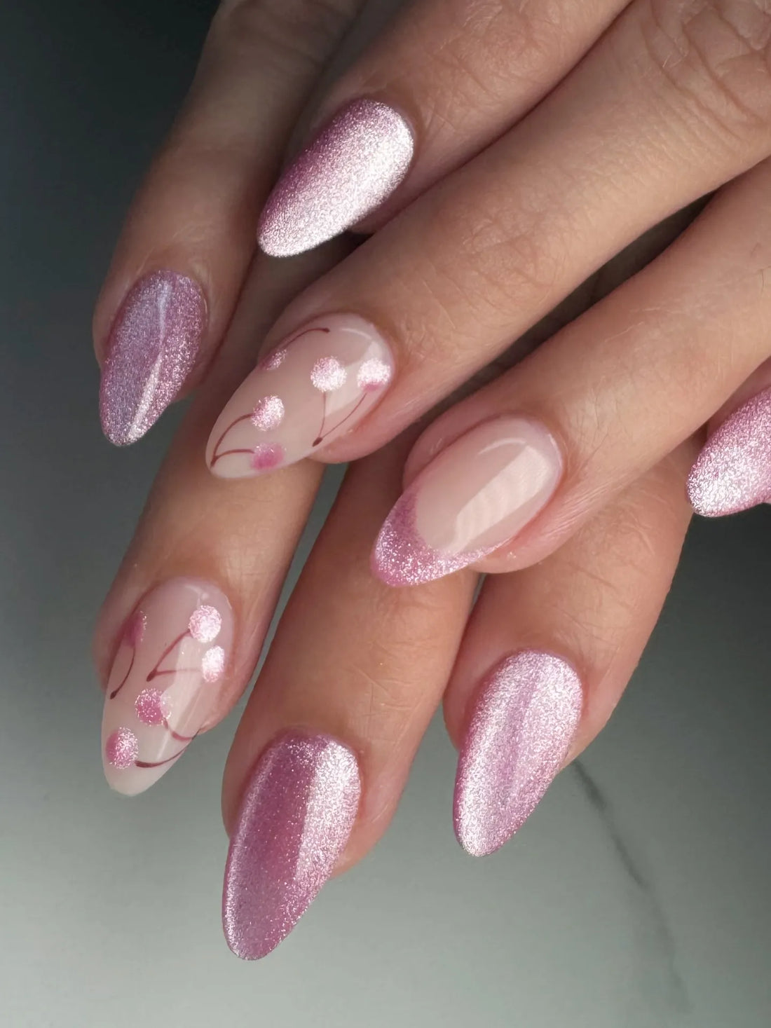 Hand with almond-shaped press-on nails in pink shimmer glitter and cherry blossom dot design