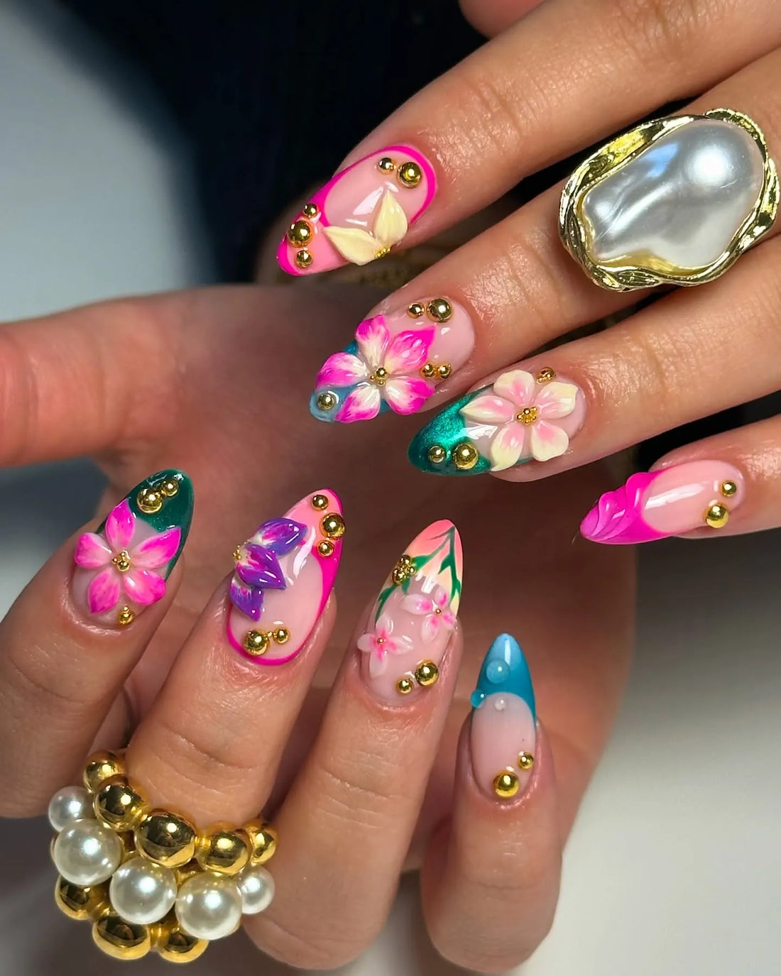 Hand with handmade pink, teal, green 3D floral press-on nails and gold accents.