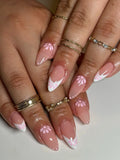 Hand with almond-shaped press-on nails featuring pink and white daisy flower French tips.
