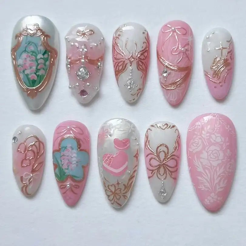 Handmade press-on nails with pink and white floral designs, rose gold foil, and jeweled accents.