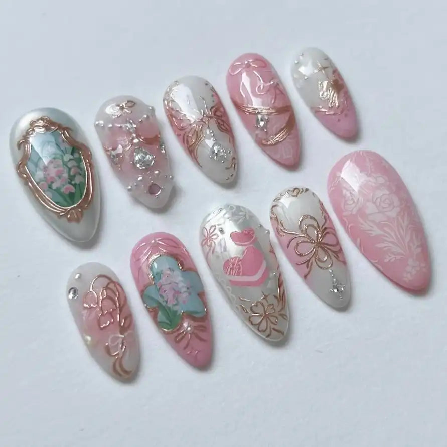 Handmade press-on nails with pink and white floral designs, rose gold foil, and jeweled accents.