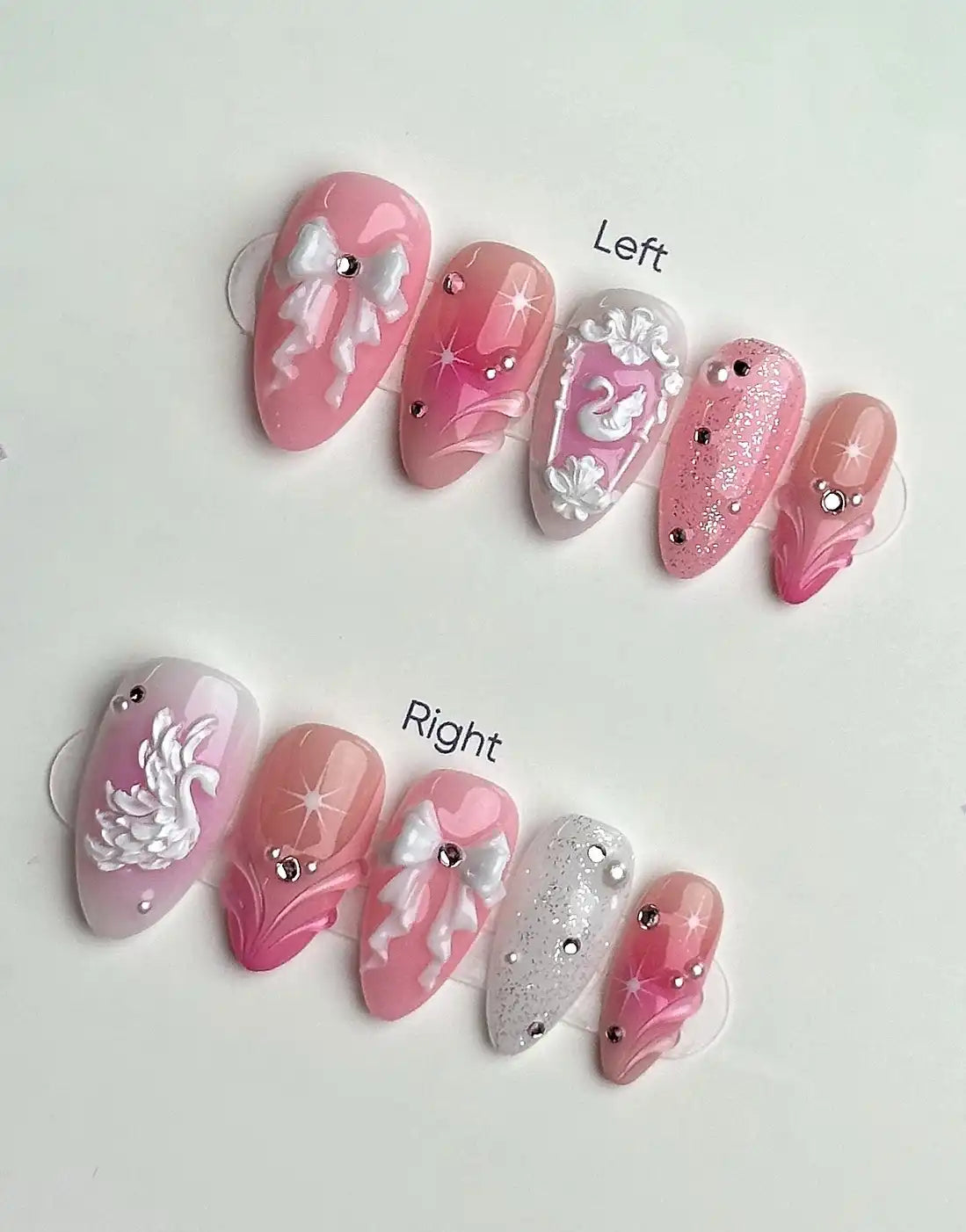 Handmade pink and white press-on nails with swan, bow, glitter, and jewel designs.