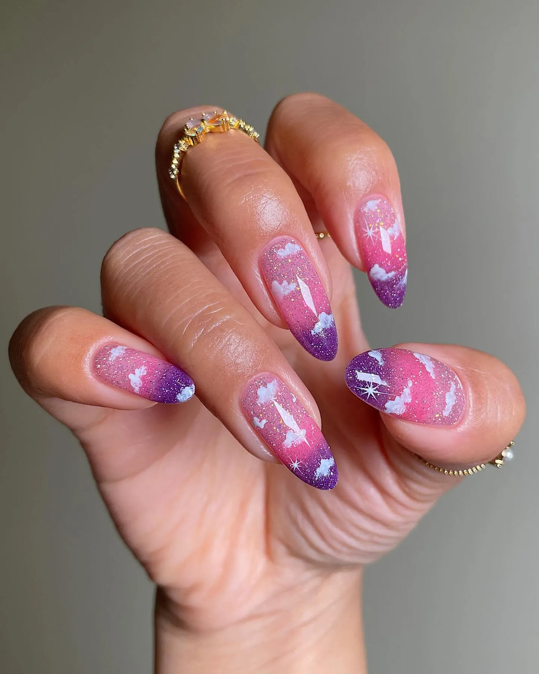 Hand with handmade pink and purple ombre press-on nails featuring cloud and glitter designs.