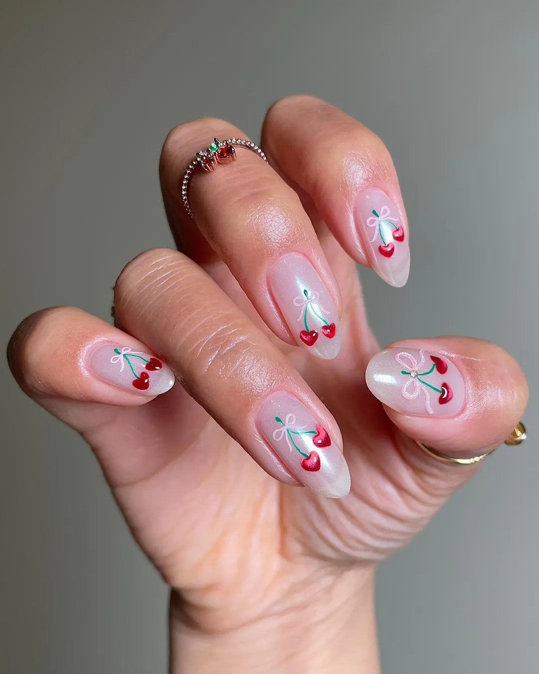 Hand holding iridescent press-on nails with red cherry bow and pearl accents, artistic design