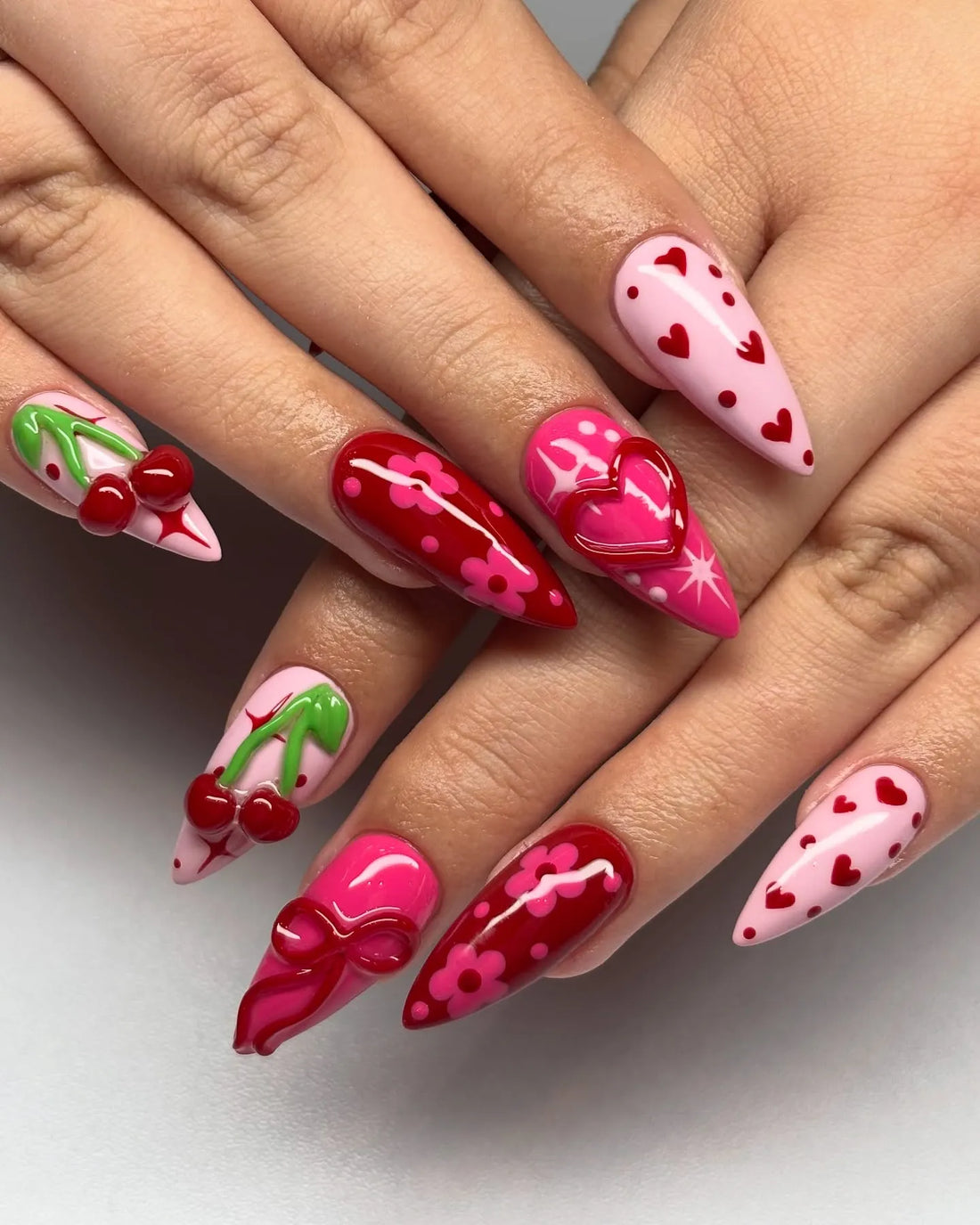 Handmade press-on nails with pink, red cherry, heart, floral, and 3D bow designs.