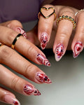 Hand with handmade nude pink press-on nails featuring red heart and floral designs