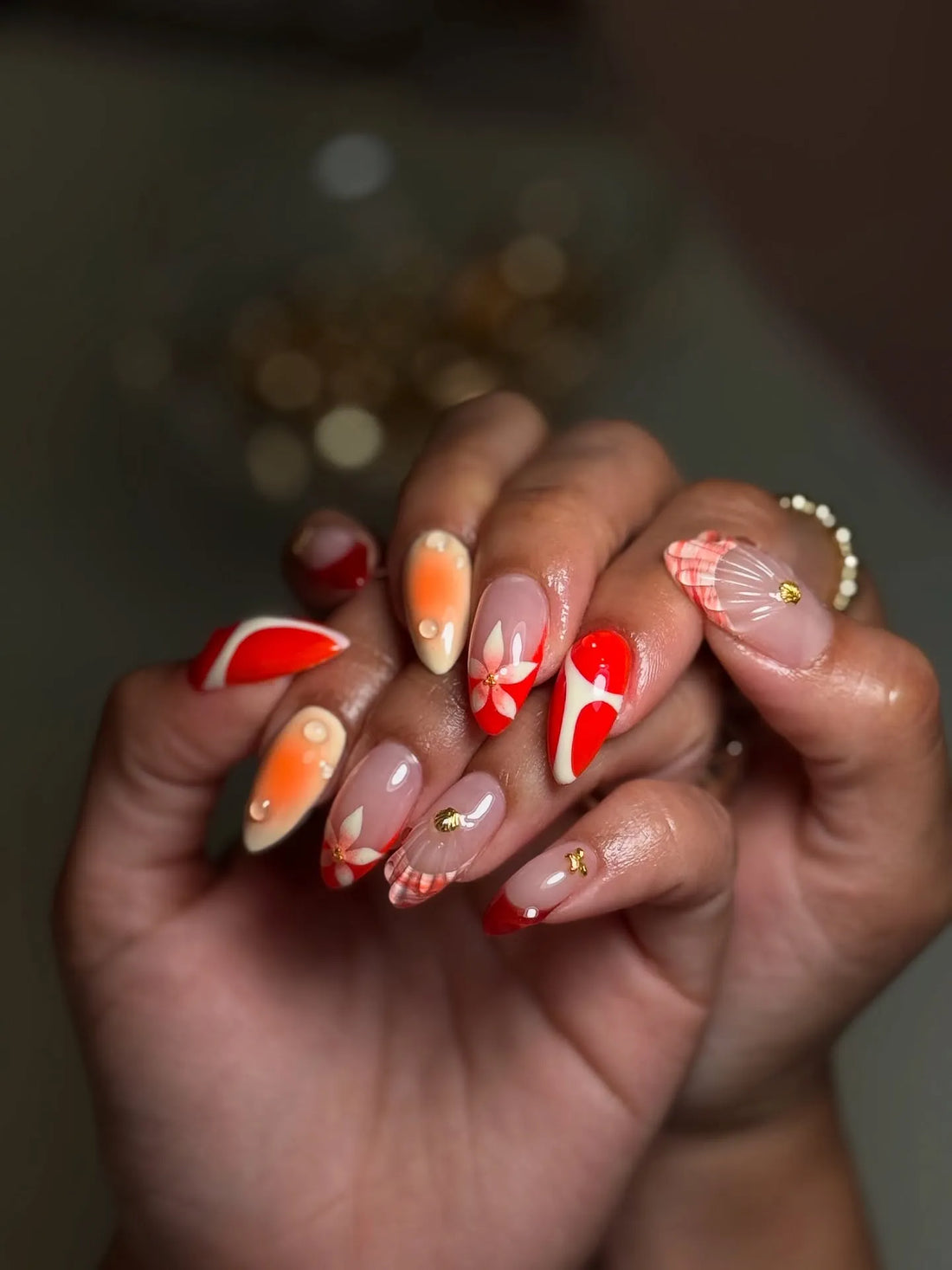 Hand with handmade red floral tropical press-on nails featuring shell and gold accents