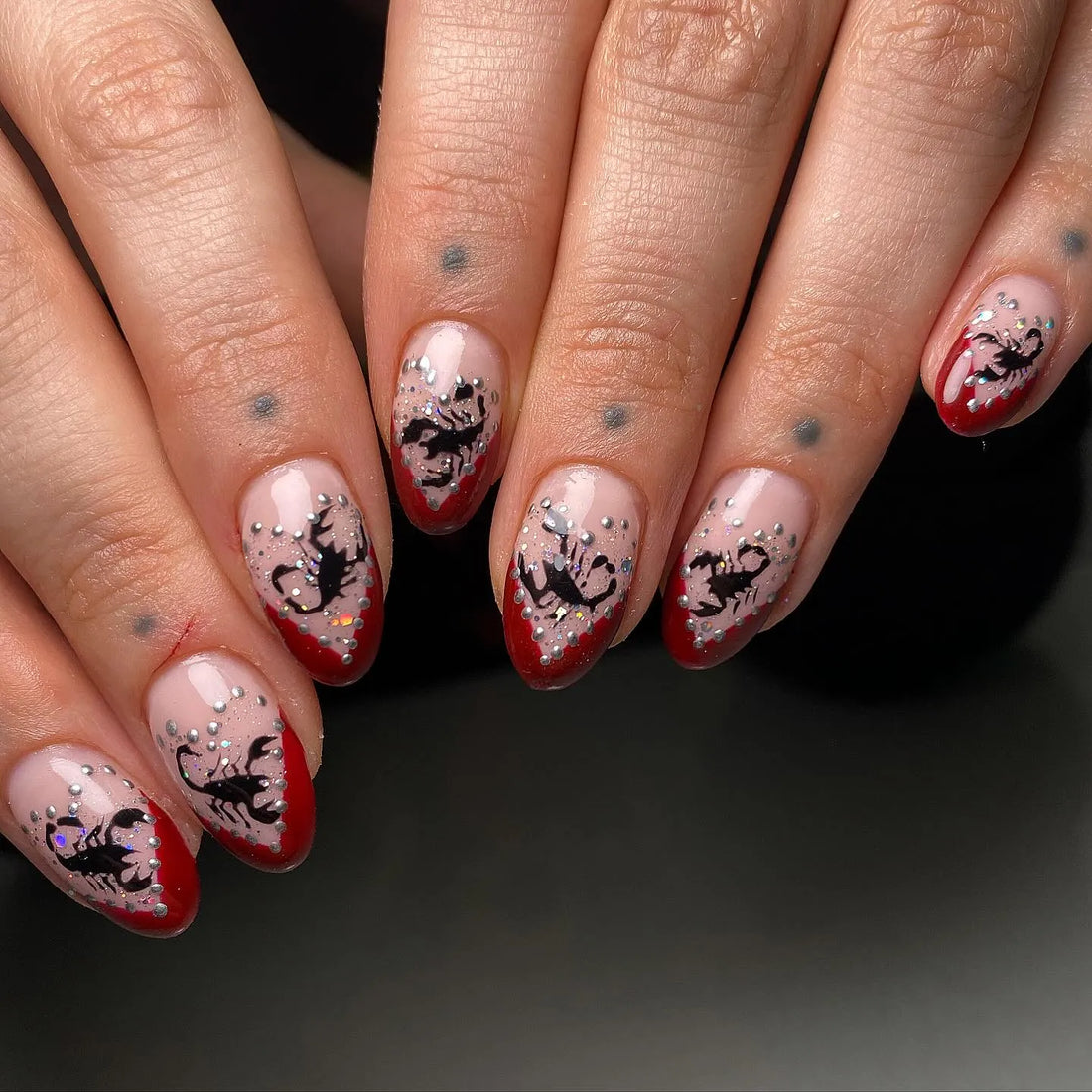 Handmade press-on nails with red French tips, black scorpion art, and silver glitter accents.
