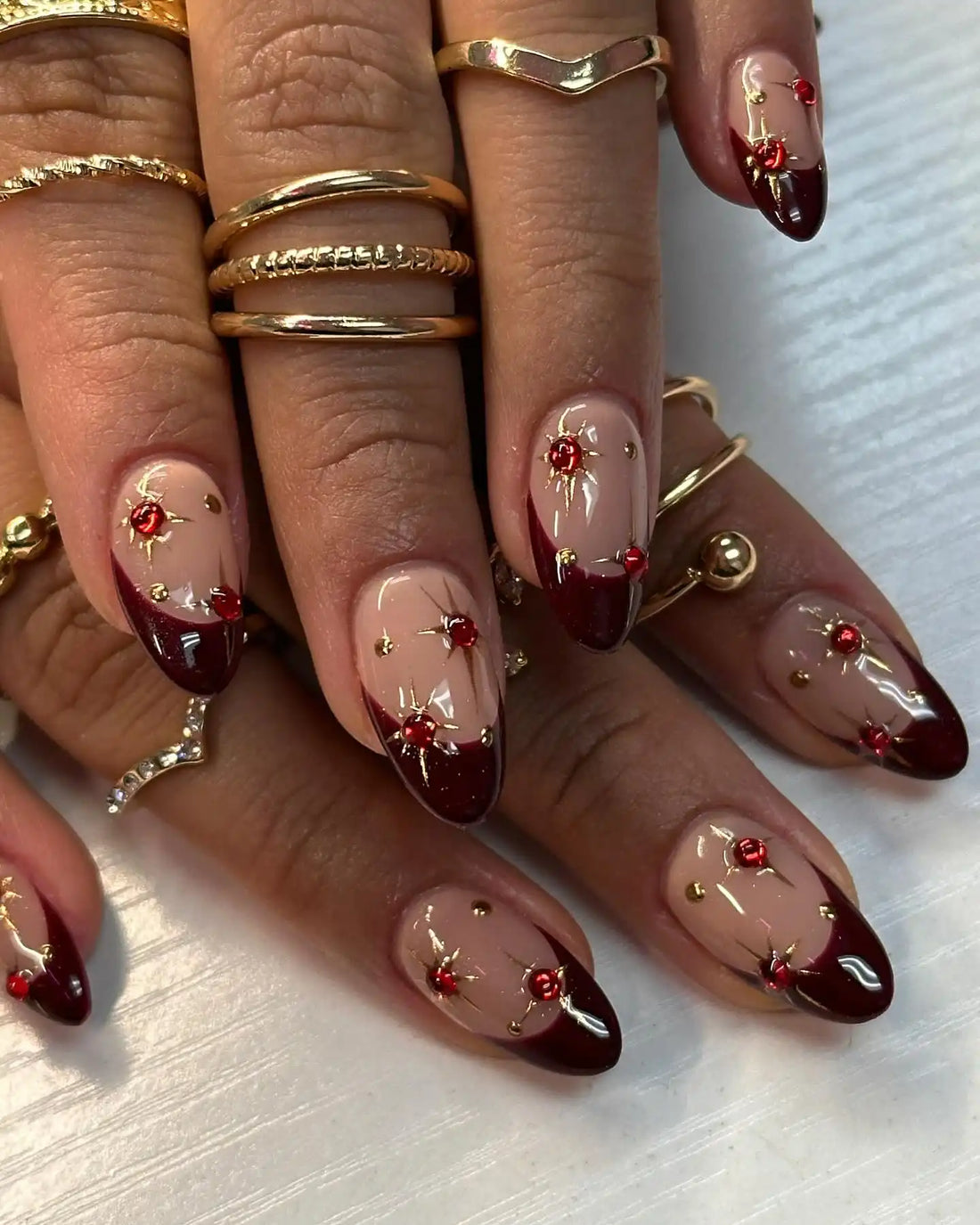 Handmade wine tip press-on nails with red gem and gold star designs on almond shape