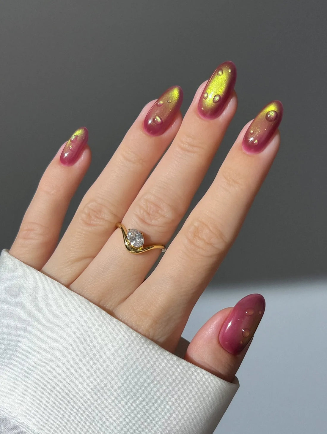 Hand wearing handmade red and gold chrome cat eye press-on nails with water drop effect.
