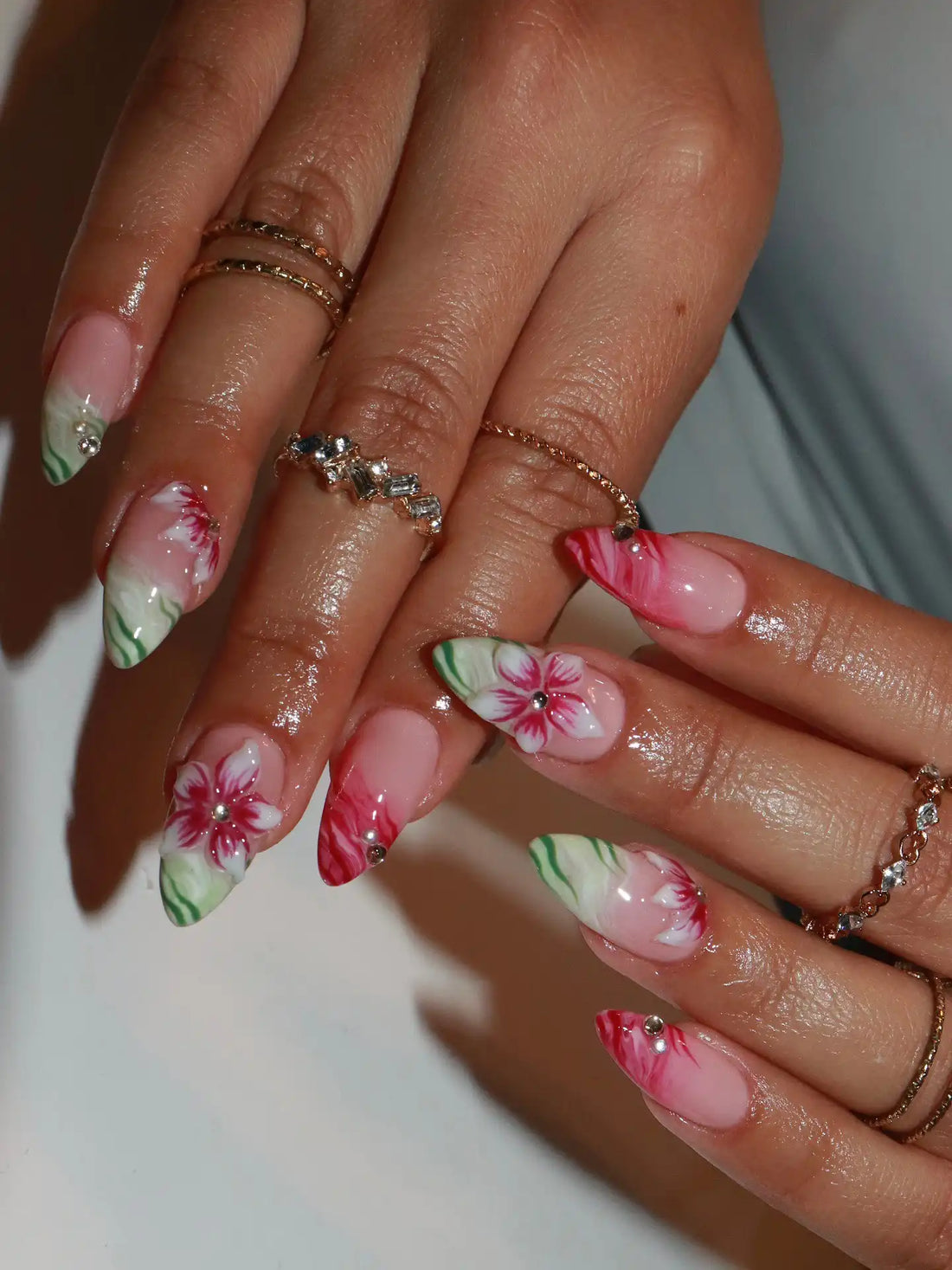 Hand with long press-on nails featuring handmade red hibiscus flower and green accents.