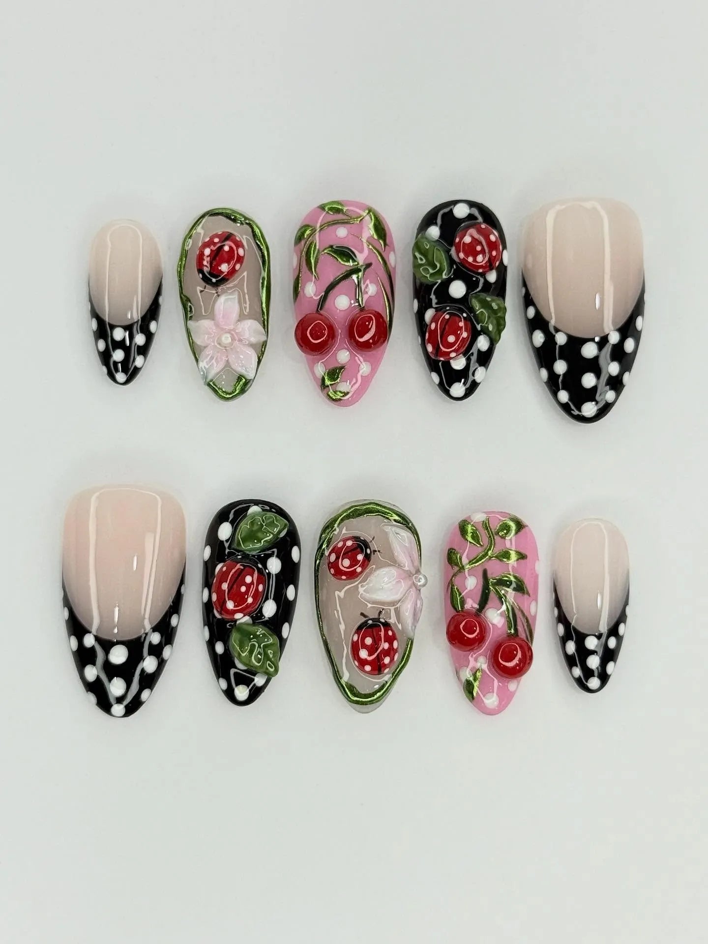Handmade press-on nails with red ladybug, cherry, floral, and black polka dot designs.