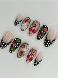 Handmade 3D press-on nails with red ladybug, cherry, and polka dot designs on black and pink.