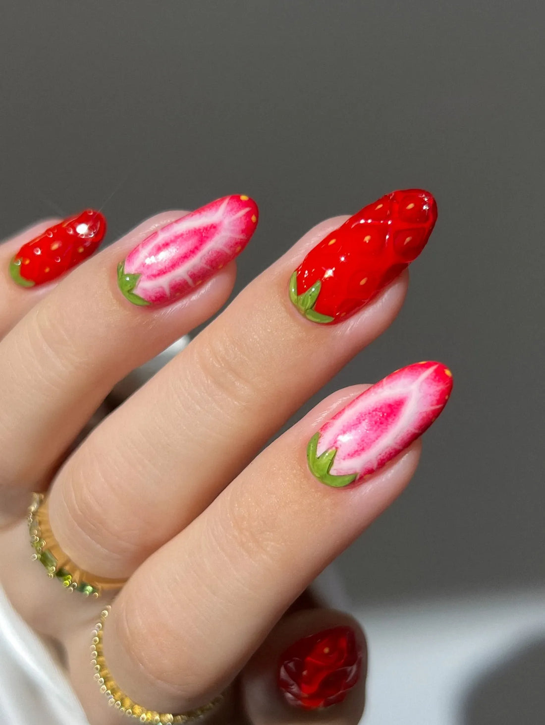 Hand with handmade red and pink strawberry fruit design cute summer press-on nails.