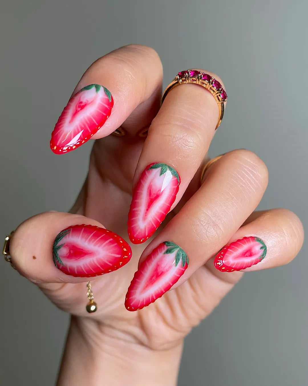 Hand holding summer fruit-themed handmade press-on nails with realistic strawberry art design.