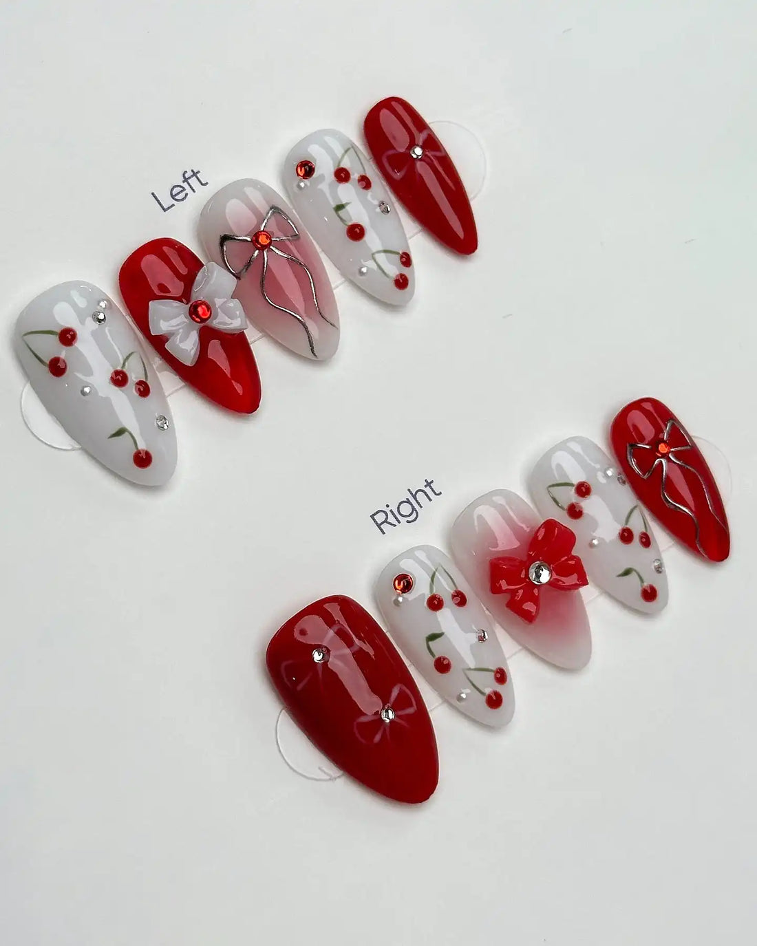 Handmade red and white press-on nails with cherry fruit, bow, and ribbon charm designs.